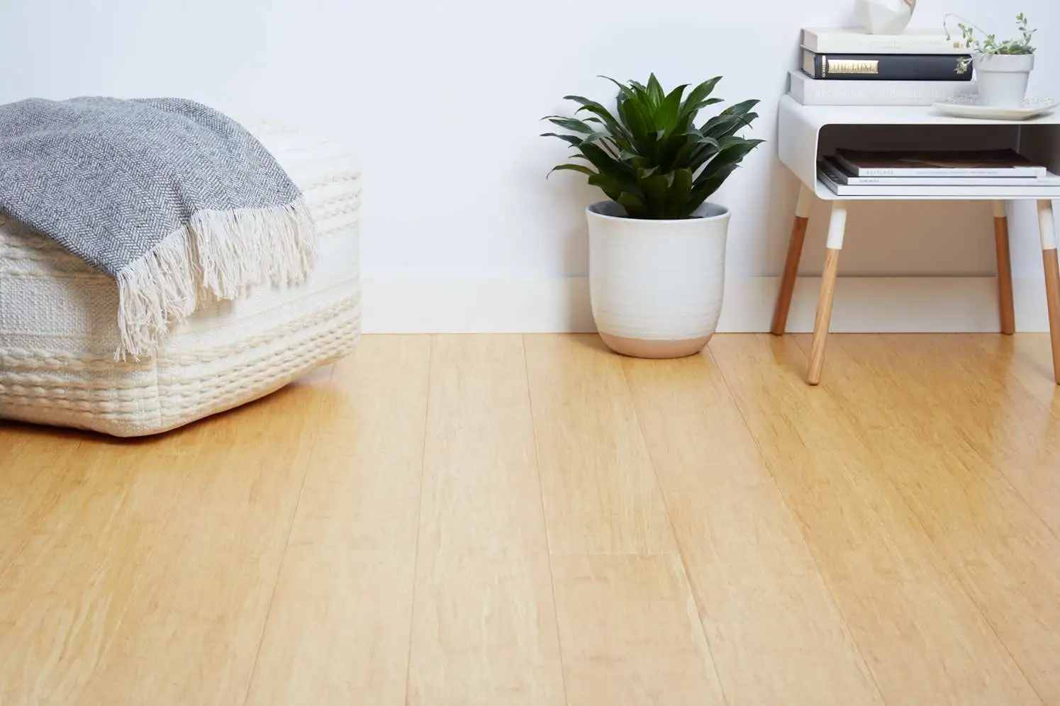 Light bamboo flooring beside pouf and plant