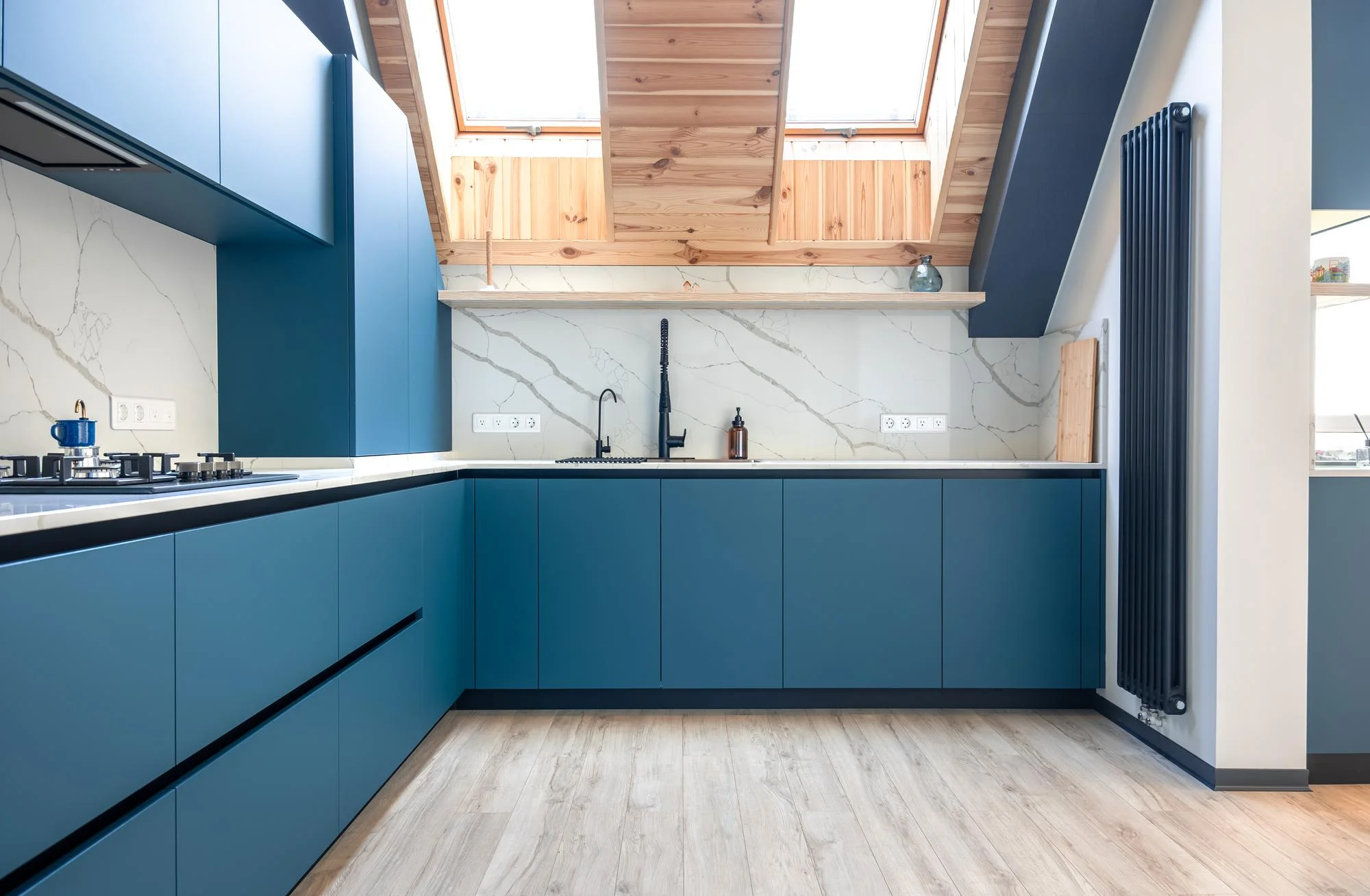 Blue modern kitchen under skylights with marble backsplash