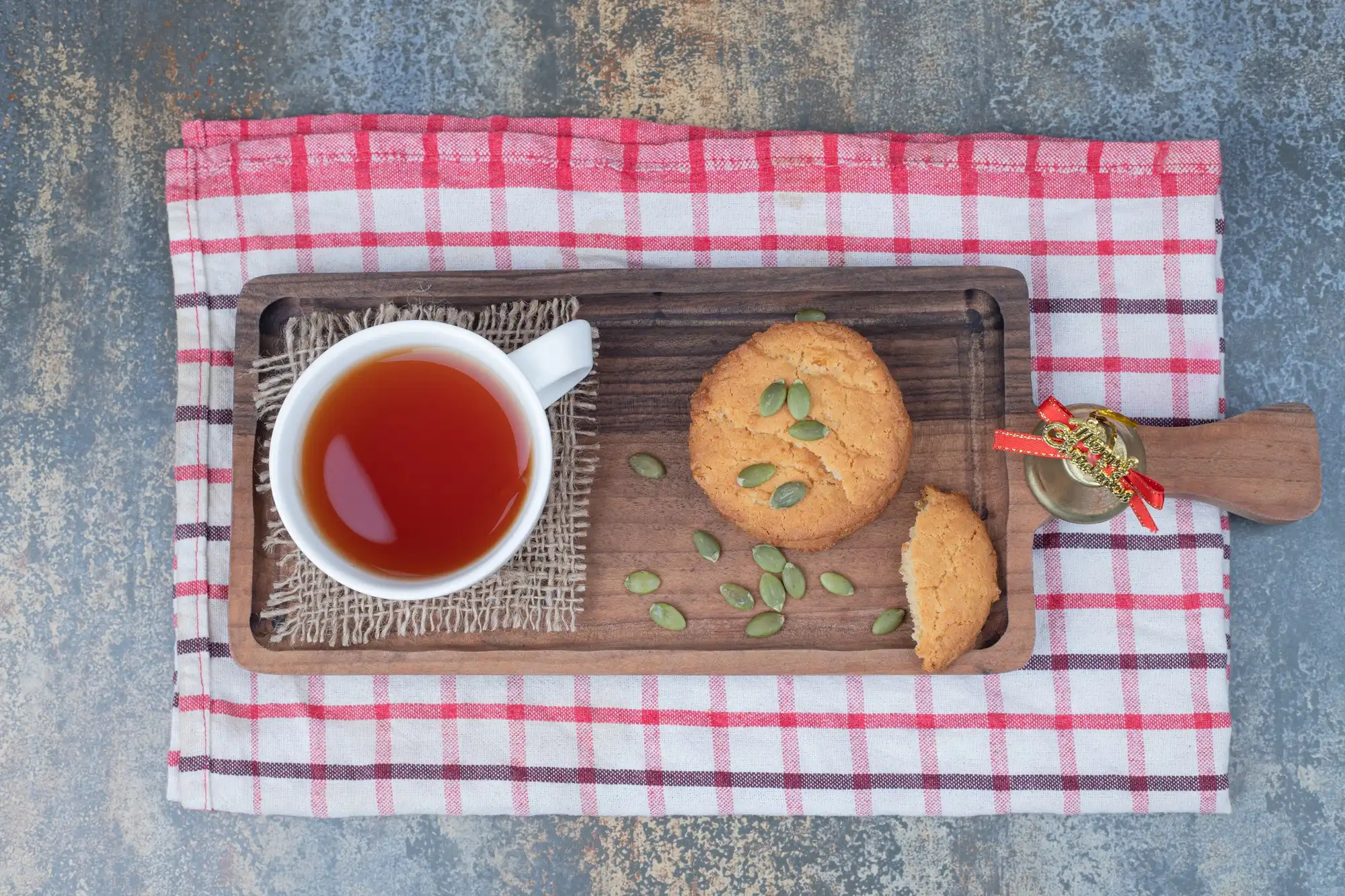 Tea cup and cookies on wooden tray with checkered towel