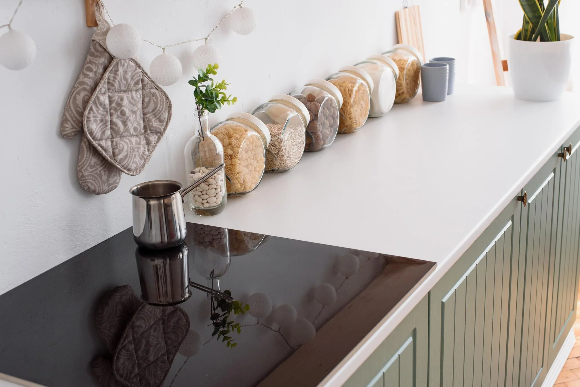 White quartz countertop with jars and a black glass cooktop