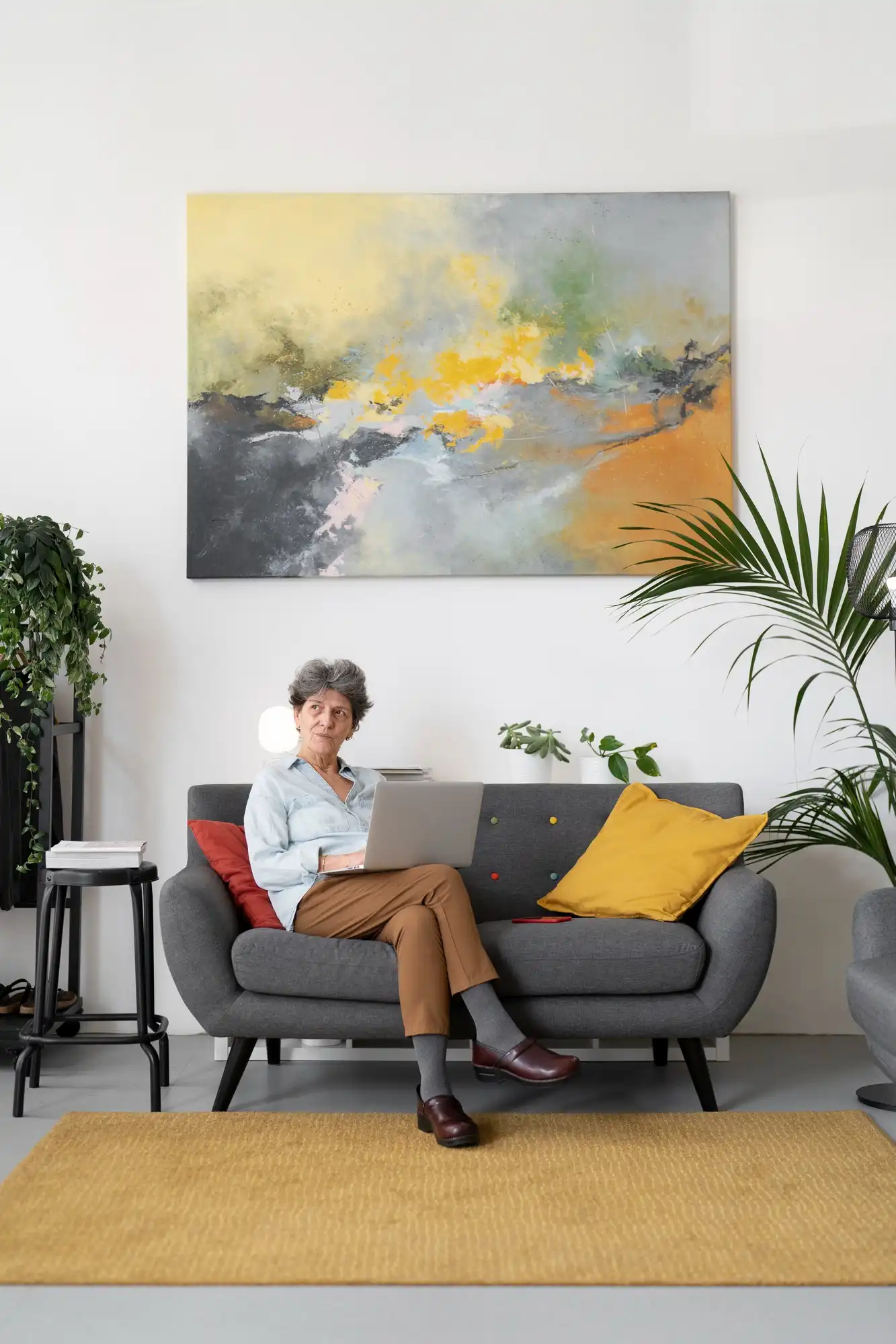 Woman on grey sofa with yellow pillow and abstract wall art