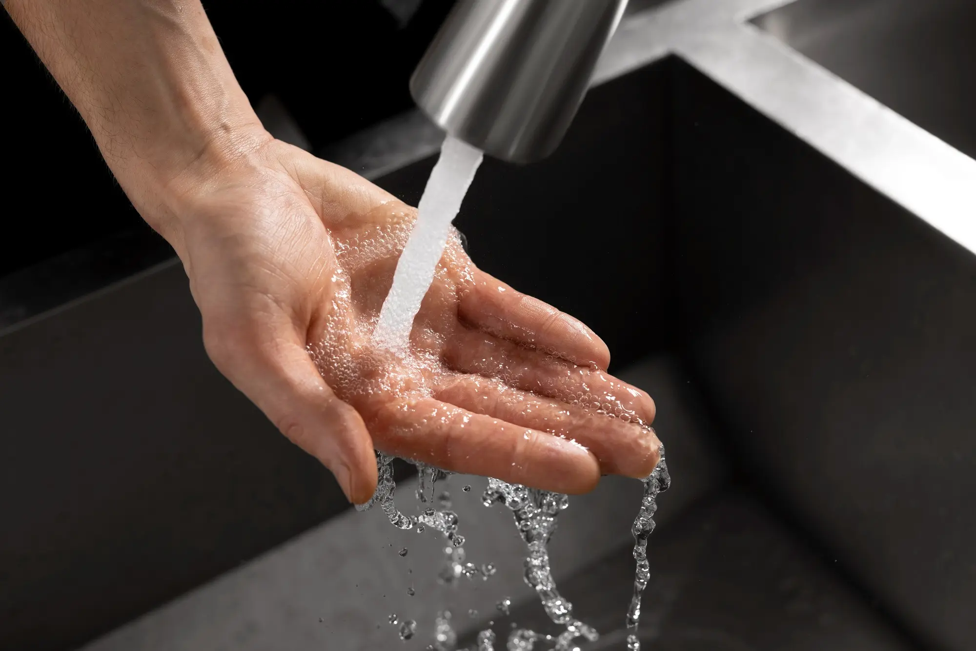 Water flowing over hand under kitchen faucet close up