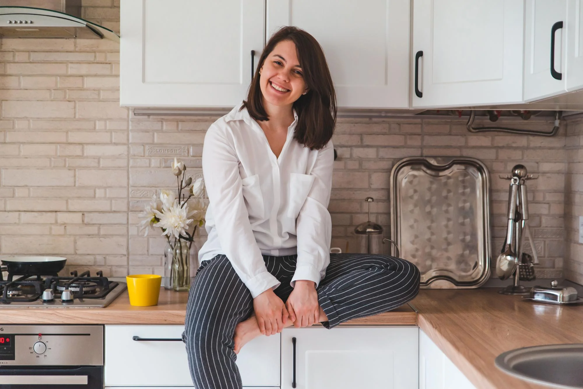 Woman sitting on countertop in bright white kitchen