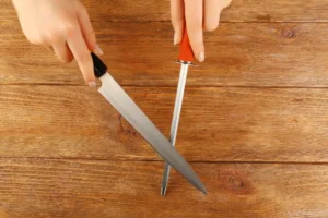Honing kitchen knife with steel rod on wooden table