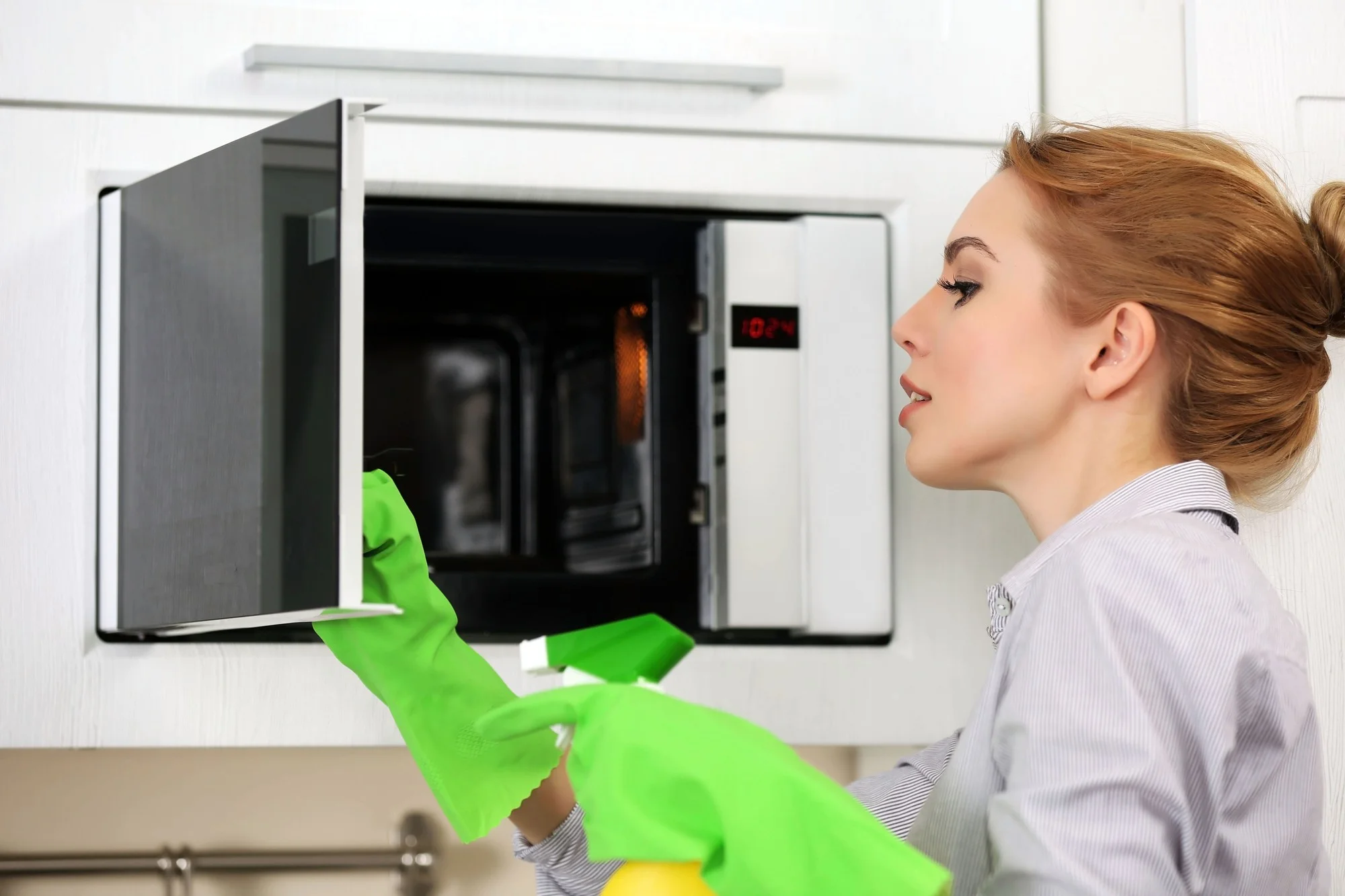 Woman cleaning microwave interior with gloves at home