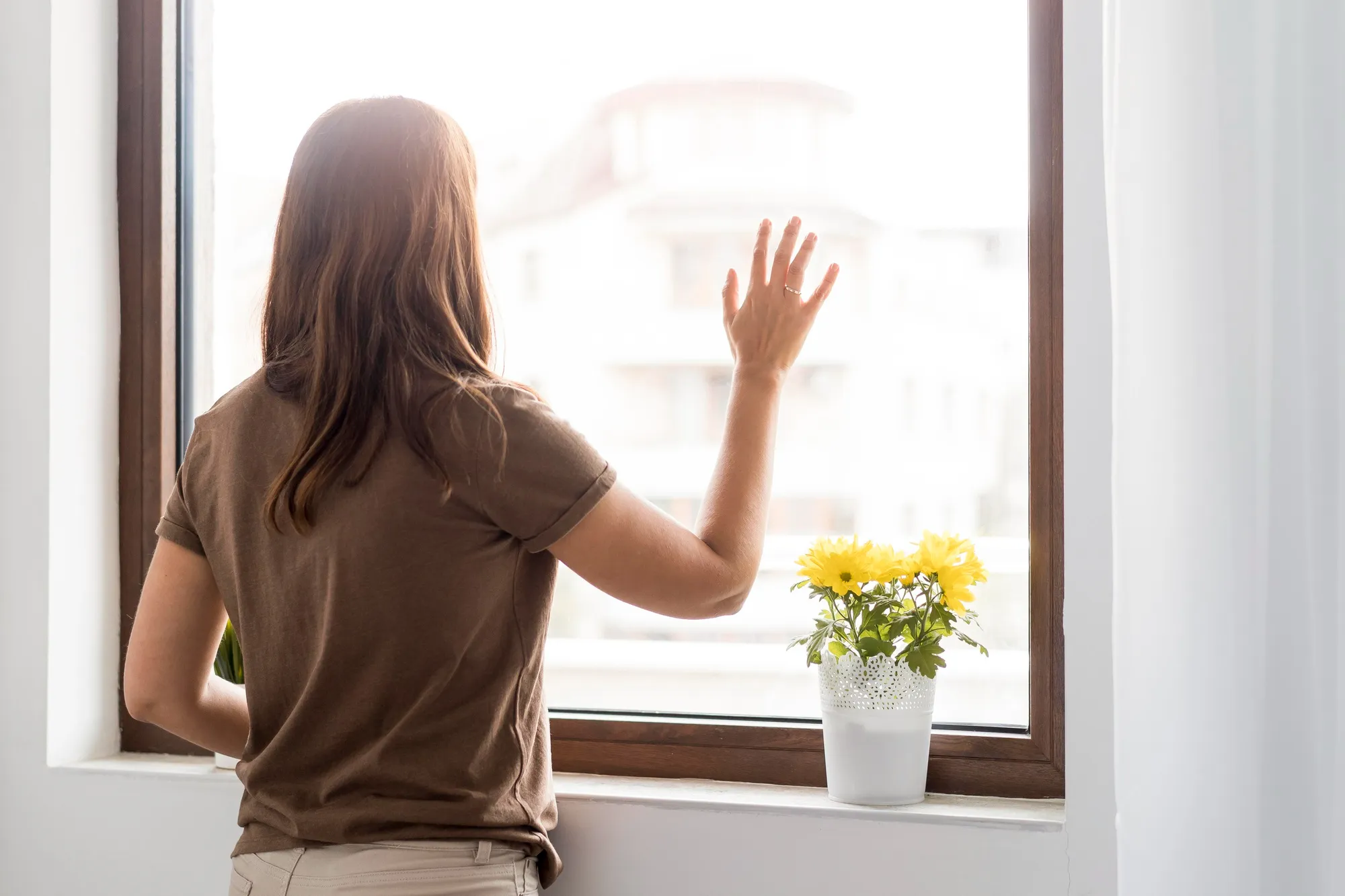 Woman checking sunlight through modern home window glass Woman checking sunlight through modern home window glass